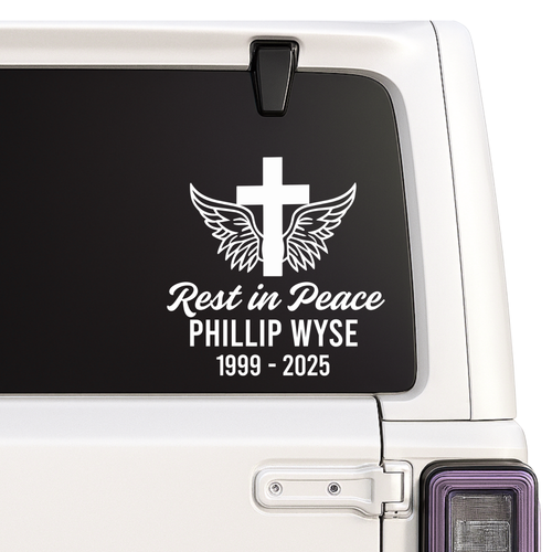 Memorial decal with cross, wings, and text on a vehicle window.