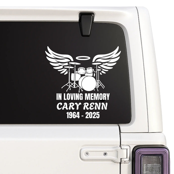 Memorial decal with drum set and wings on a vehicle window.