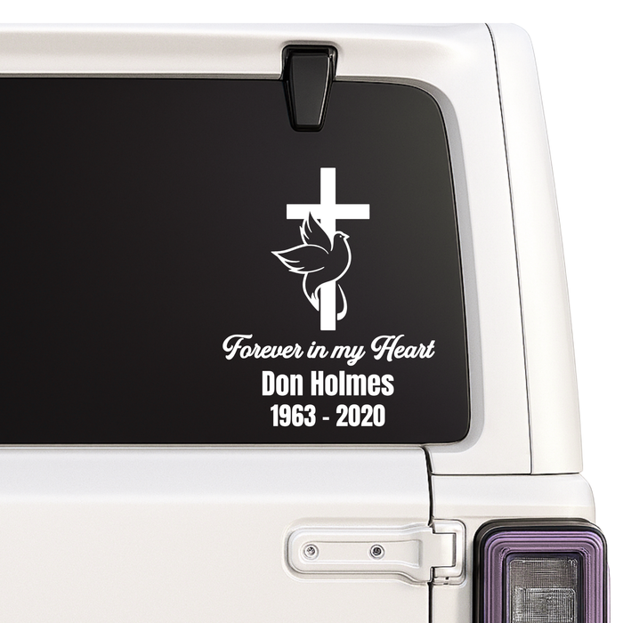 Memorial decal with cross, dove, and text on a vehicle window.