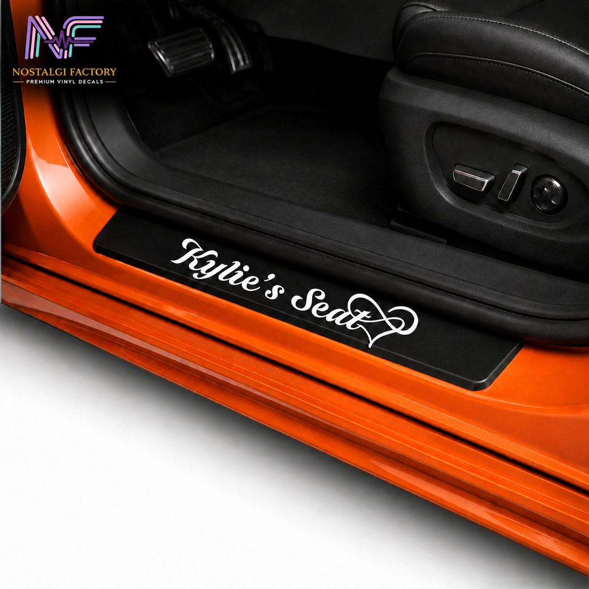 A black car door sill mat with white script text reading 'Kylie's Seat' and a heart design, shown installed on the door sill of an orange car interior.