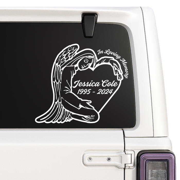 Memorial decal of an angel holding a heart with engraved text on a vehicle window.